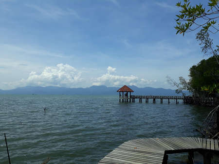 Waterfront promenade and pavilion that extends to the middle of the sea. Behind is a mountain view with a clear sky.の写真素材