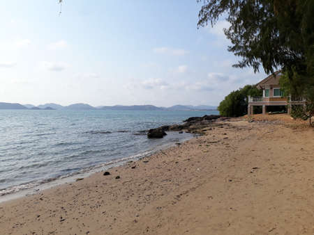 A sandy beach with a tree front In the back there is a house in the shape of a square.の写真素材