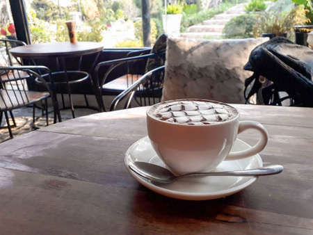 Hot chocolate decorated with whipped cream on a wooden table in a cafe outside the cafe is a garden.の写真素材