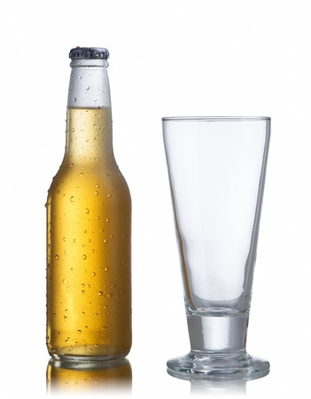 Non-glossy white beer bottle, back lighted showing a glowing golden beer content, drops and condensation and an empty glassの写真素材