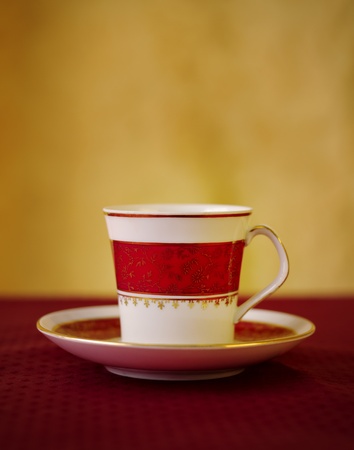 Vintage coffee cup with red and gold patterns over red carpet against yellow background. Copy space over the cup. Thin focus to emphatice the depth of the image giving a warmer and personal feeling.の写真素材