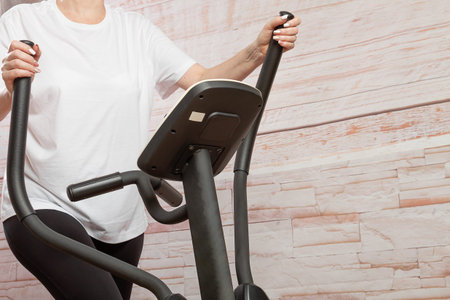 A middle-aged woman goes in for sports on an elliptical trainer at home.