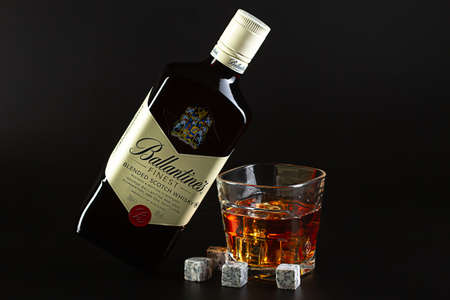 Israel. Rishon LeZion. 08.14.2021. A bottle of Ballantines whiskey lies on its side on a glass of whiskey with ice and whiskey stones against a black background.のeditorial素材