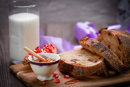 Honey, pomegranate, milk and bread on a wooden cutting board.