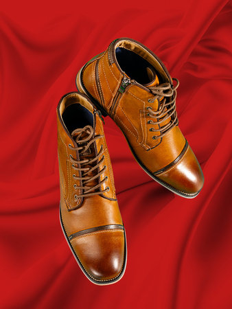 A pair of premium calfskin boots on a red background. Vertical shot. Men's shoe ideas.