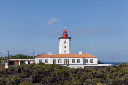White lighthouse built on volcanic rocks with blue sky background at Pico Island, Azoresの写真素材