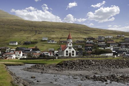 Sandavagur Church with red roof also called Sandavags Kirkja and the river Stora located in the picturesque village of Sandavagur on Faroe Islands, Denmarkの写真素材