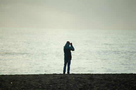 Black sand beach, Vik, Iceland - 4 November 2016: Sole tourist taking picture on the seashore in...