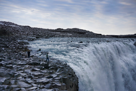 Peoples small figures in comparison with Dettifoss waterfall covered with ice, Iceland