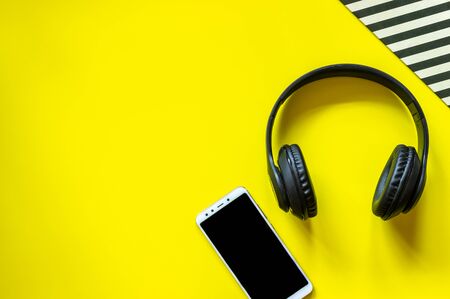 Black headphones and a phone on a yellow background. Minimal concept. Design. Flat layの写真素材