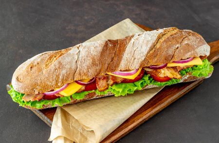 A sandwich of dark bread with salad, bacon, tomatoes, cheese and onions. Baguette. Breakfast. Fast food. Healthy eating. Recipes.の写真素材
