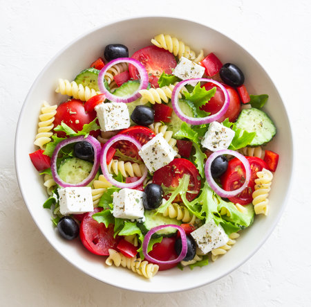 Greek pasta salad with feta cheese, tomatoes, onion, cucumbers, peppers and olives. Healthy eating. Vegetarian foodの写真素材