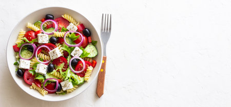 Greek pasta salad with feta cheese, tomatoes, onion, cucumbers, peppers and olives. Healthy eating. Vegetarian foodの写真素材