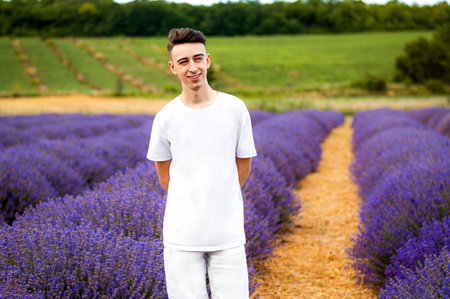 A young guy with a smile in a white shirt stands in a lavender fieldの写真素材