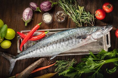 Fresh uncooked fish with lemon, herbs, vegetables and spices on rustic wooden board over brown backdrop, top viewの写真素材