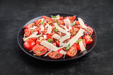 Side view of tomato salad with parmesan in a black plate on a dark stone backgroundの写真素材