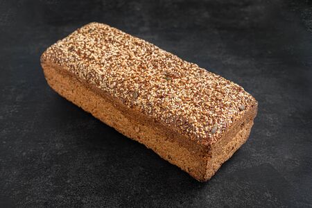 Bakery products. Crispy, wholegrain bread on a dark background. Wheat bread with flax and sunflower seeds. Side view.の写真素材