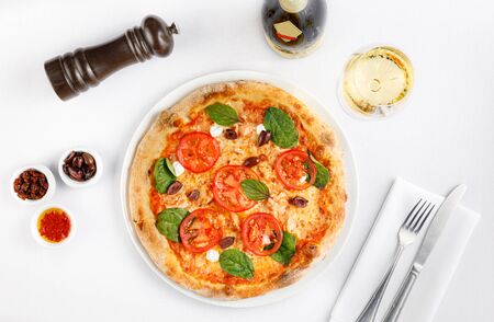 Delicious pizza, tomatoes, olives, bottle of white wine on white background, top view. Fine dining concept.の写真素材
