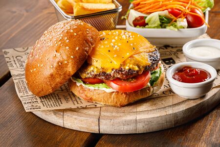 Cheeseburger, salad, potato chips and ketchup on a wooden tray.の写真素材