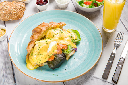 Eggs Benedict Breakfast Plate with Salmon and Croissant, Gourmet Lunch: Tasty Fried Eggs and Toasted Croissant, Healthy Brunch Salad with Fresh Vegetables.の写真素材