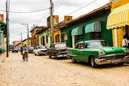 Trinidad, Cuba - 2019.Cuban riding a bicycle and old automobiles parked in front of colorful houses on the cobblestone streets of the UNESCO World Heritage old town in Trinidad, Cuba.のeditorial素材
