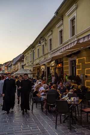 Brasov, Romania - 2019. People having dinner and priests wandering on the streets of Brasov old town.のeditorial素材