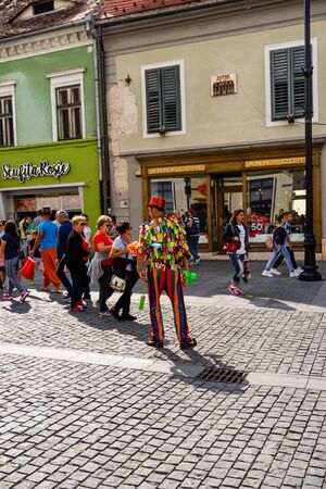Sibiu, Romania - 2019. Man wearing colorful clothes and blowing up balloons for entertainment of people in the old town.のeditorial素材
