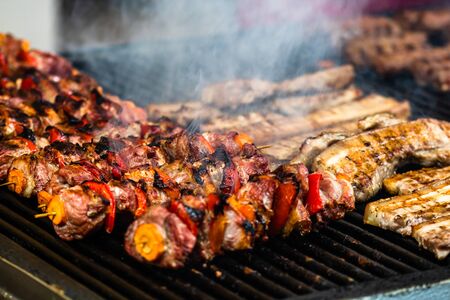 Juicy steaming meat on a charcoal grill, pork steaks, chicken breast, sausages, pieces of meat chops at a street food festivalの写真素材