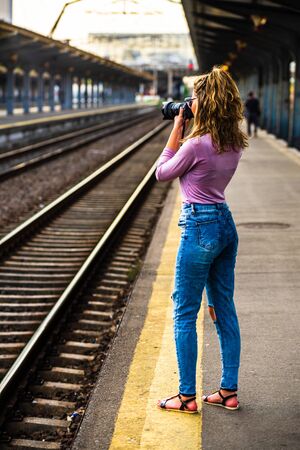 Young girl walking alone on train platform and taking photos on railway stationの写真素材