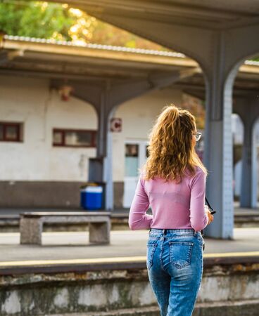 Young girl walking alone on train platform and taking photos on railway stationの写真素材