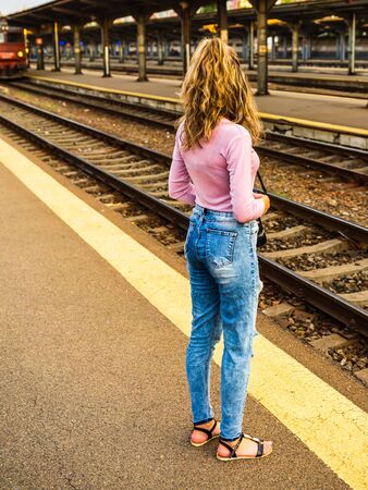 Young girl walking alone on train platform and taking photos on railway stationの写真素材