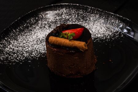 Chocolate mousse with strawberry and chocolate stick on a black dish.の写真素材