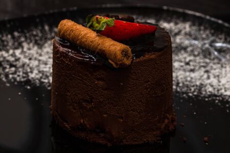 Chocolate mousse with strawberry and chocolate stick on a black dish.の写真素材