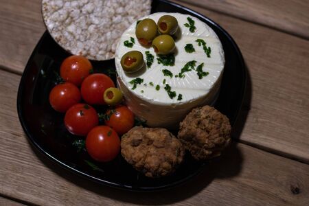 Breakfast dish (cheese, meatballs, green olives, cherry tomatoes, rice crackers) on a rustic wooden plank board table background.の写真素材