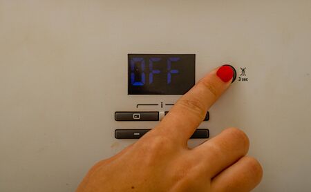 Woman hand try to turn off and on the central heating in the room. Female hands on the central heating control panel. Girl hand setting temperature to heating system.の写真素材