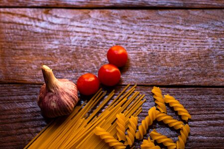 Spaghetti, cherry tomatoes and garlic on a wooden board.の写真素材