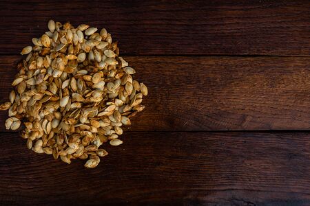 Roasted and salted pumpkin seeds on a wooden board.の写真素材