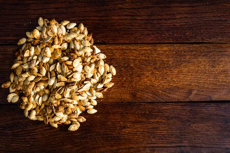 Roasted and salted pumpkin seeds on a wooden board.の写真素材
