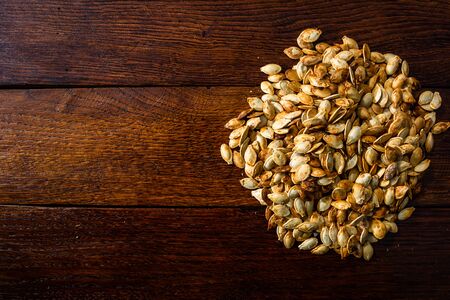 Roasted and salted pumpkin seeds on a wooden board.の写真素材