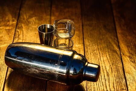 Cocktail shaker accessories and shots glasses on a wooden board.の写真素材