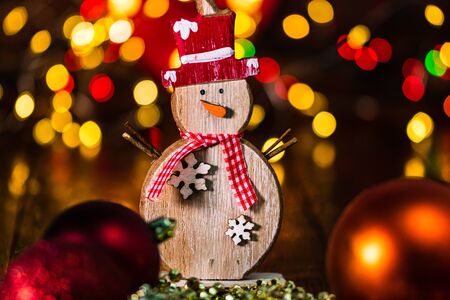 Christmas decorations against blurred background and out of focus lights. Decorative wooden snowman and glittery Christmas ballsの写真素材