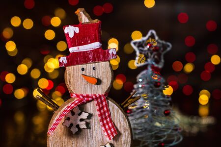 Christmas decorations against blurred background and out of focus lights. Decorative wooden snowman and glittery Christmas ballsの写真素材