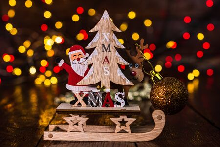 Christmas decorations against blurred background and out of focus lights. Close up of a wooden Christmas sledge with Santa Claus, a reindeer, Christmas tree and glittery Christmas ballsの写真素材