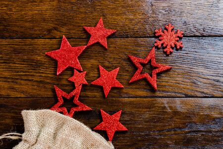 Christmas burlap sack with glittery and shiny Christmas decorations. Christmas decorations on wooden board. Red Christmas stars and snowflakes.の写真素材