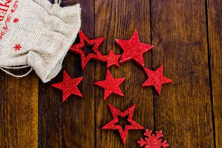 Christmas burlap sack with glittery and shiny Christmas decorations. Christmas decorations on wooden board. Red Christmas stars and snowflakes.の写真素材