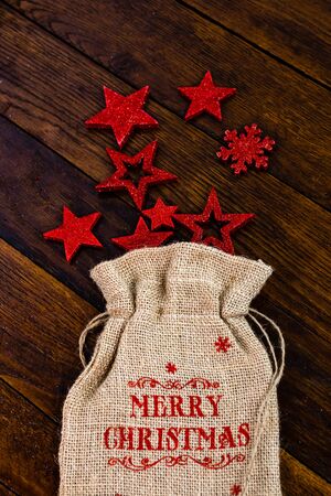 Christmas burlap sack with glittery and shiny Christmas decorations. Christmas decorations on wooden board. Red Christmas stars and snowflakes.の写真素材