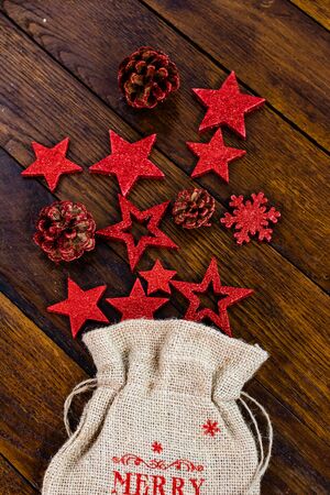 Christmas burlap sack with glittery and shiny Christmas decorations. Christmas decorations on wooden board. Red Christmas stars and snowflakes.の写真素材