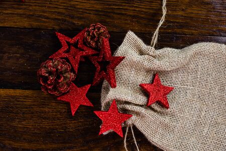 Christmas burlap sack with glittery and shiny Christmas decorations. Christmas decorations on wooden board. Red Christmas stars and snowflakes.の写真素材