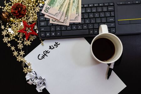 Different objects on black office desk. Modern black office desk table with keyboard, Gift list, Dollars money, cup of coffee and Chrsitmas decorations.の写真素材