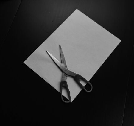 Black and white photo. Scissors on blank A4 paper. Blank paper with scissors on black office desk.の写真素材